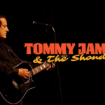 Promotional poster for Tommy James & The Shondells. Pictured is Tommy James playing guitar. Against a dark background, in yellow and orange it reads "Tommy James & The Shondells."