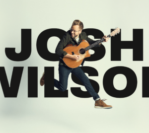 Josh Wilson holding guitar and jumping in mid air in front of text "Josh Wilson".